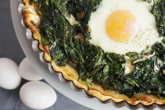 Die Tarte mit der Spinat-Masse und ausgesparten Mulden wird zunächst 20 Minuten gebacken. Die Tarte mit der Spinat-Masse und ausgesparten Mulden wird zunächst 20 Minuten gebacken.
