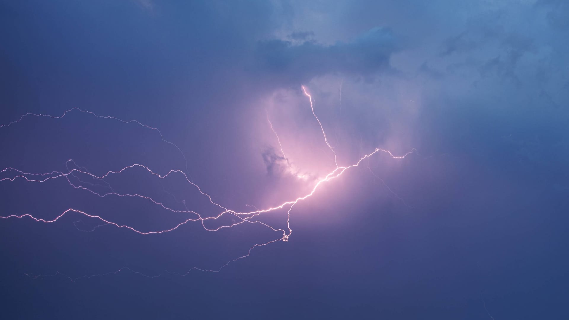Blitze zucken am Himmel neben dunklen Gewitterwolken (Archivbild): In Köln und der Region drohen ab Dienstag starke Unwetter.