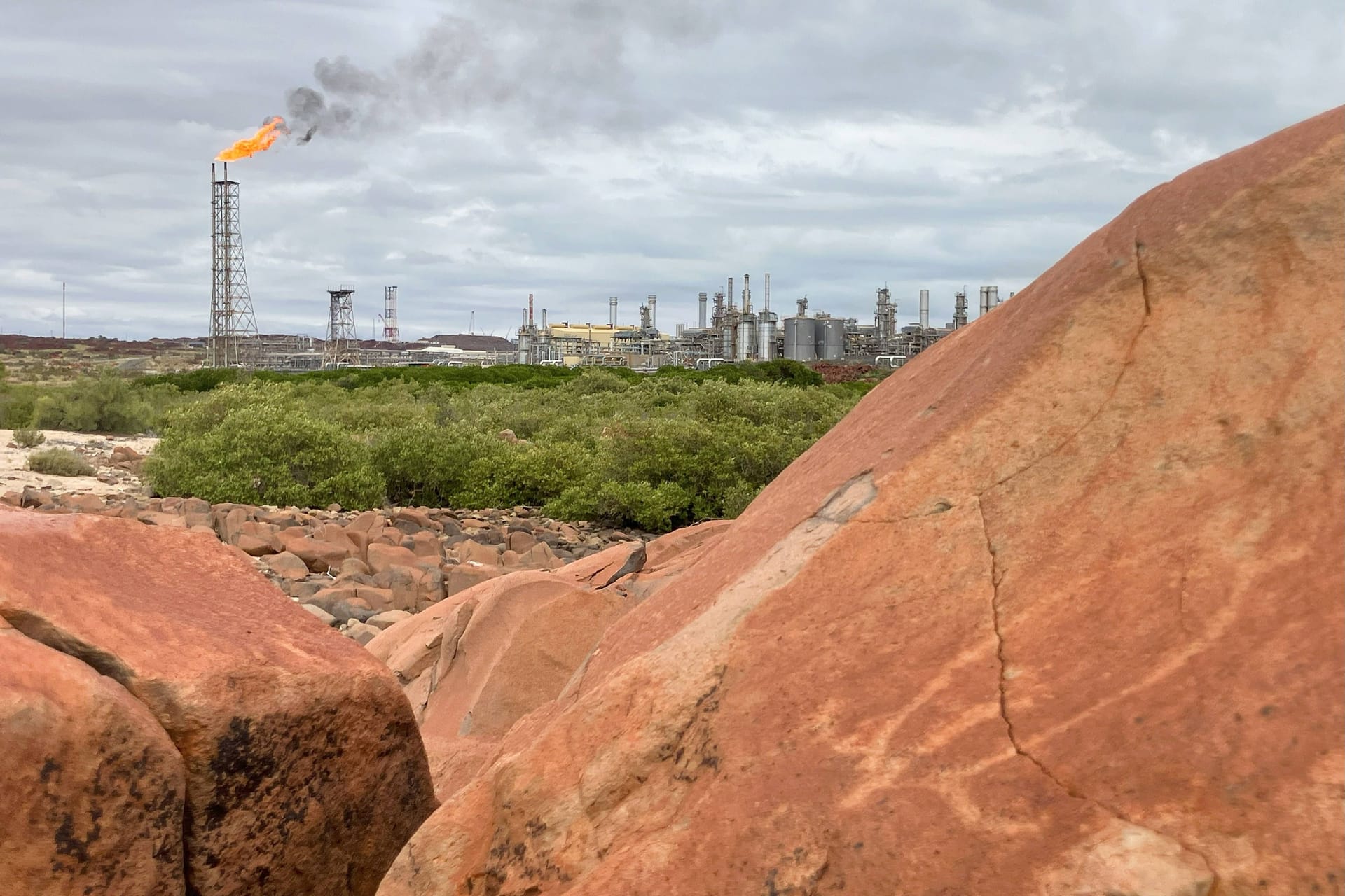 Ein Murujuga-Felsen mit Schildkrötendarstellung: Im Hintergrund brennt die Flamme einer Raffinerie. Ein Murujuga-Felsen mit Schildkrötendarstellung: Im Hintergrund brennt die Flamme einer Raffinerie.